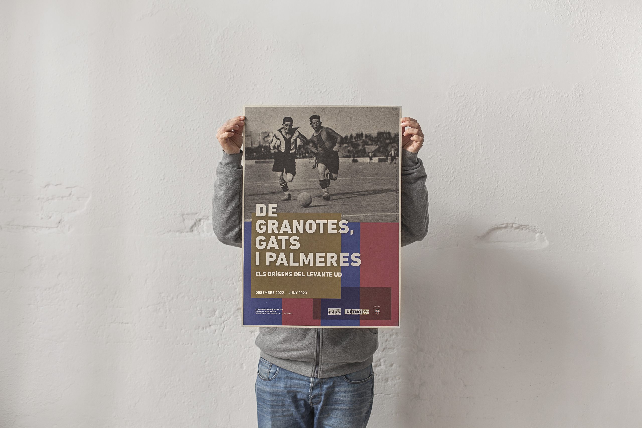 Persona sujetando el cartel de «DE GRANOTES, GATS I PALMERES. Els orígens del Levante UD»